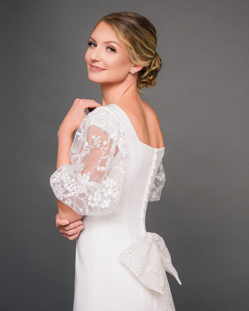 Woman wearing a ivory modest lace dress against a gray background