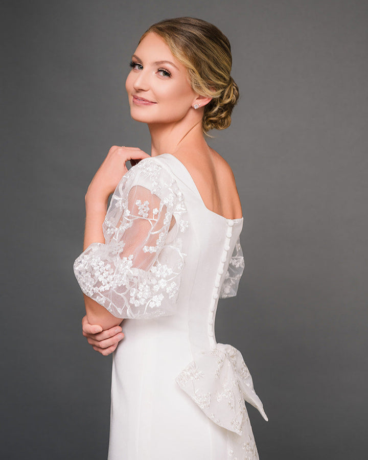 Woman wearing a ivory modest lace dress against a gray background