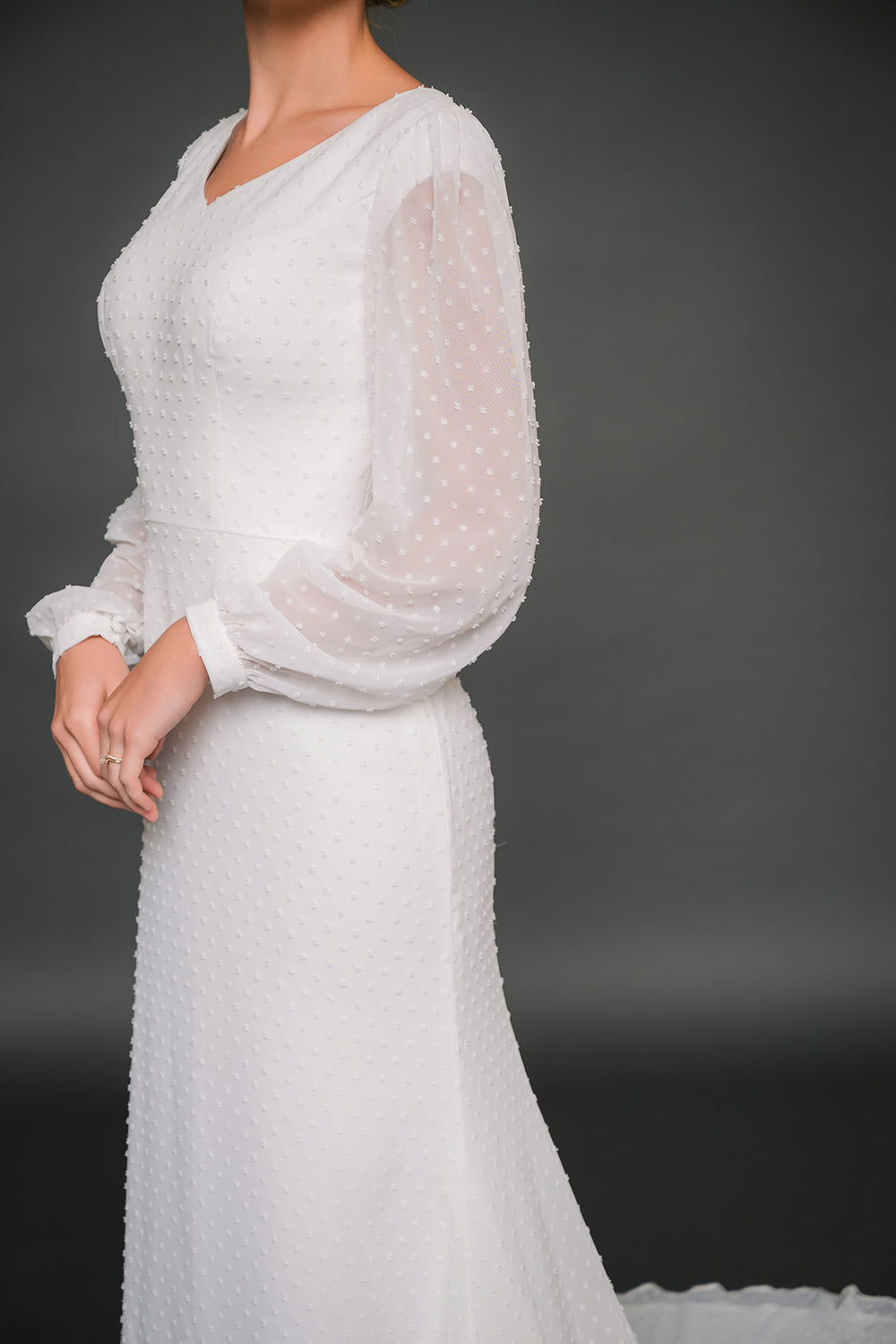 ivory chiffon modest wedding dress with sheer sleeves on a dark background