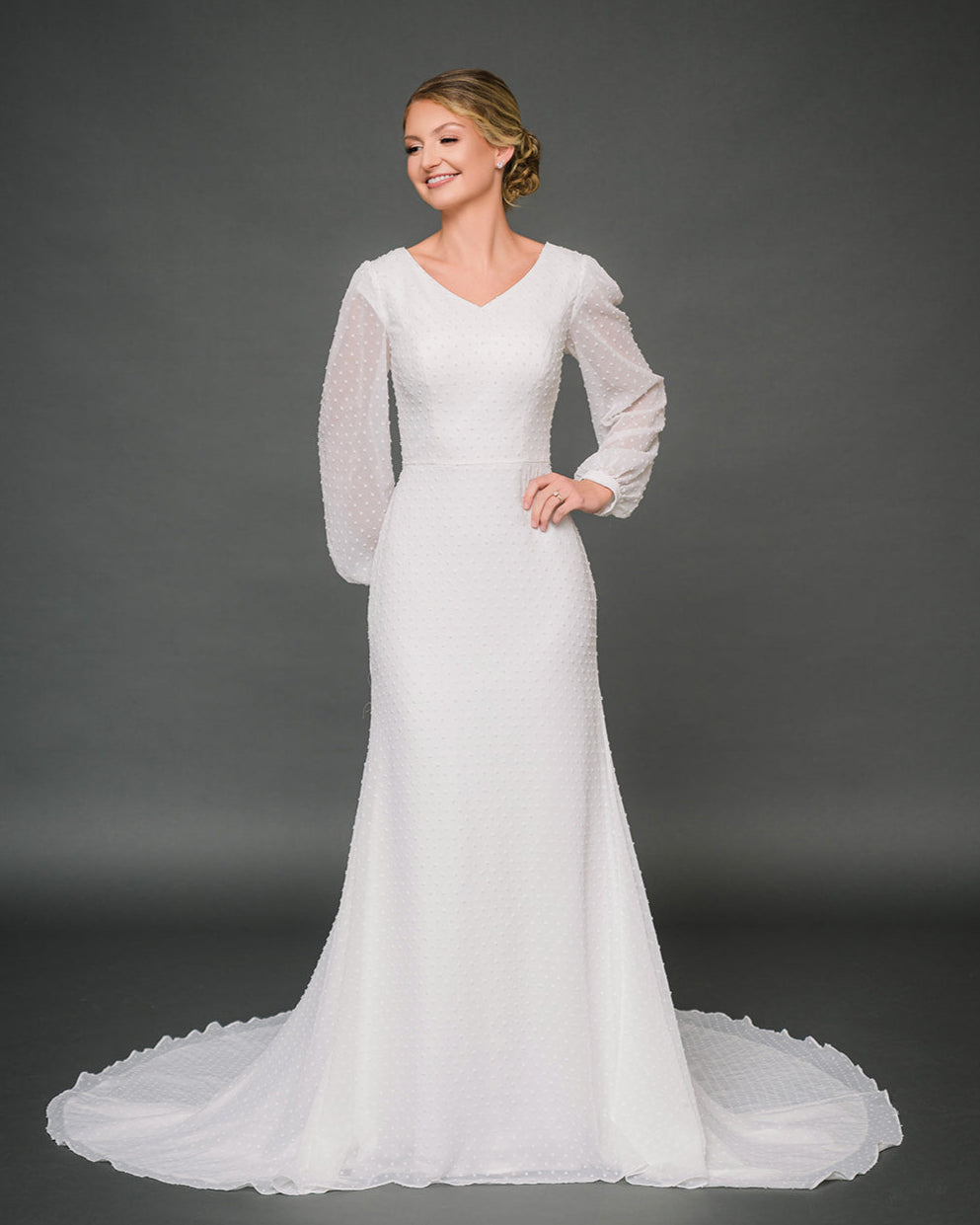 Woman wearing a white modest wedding dress against a gray background