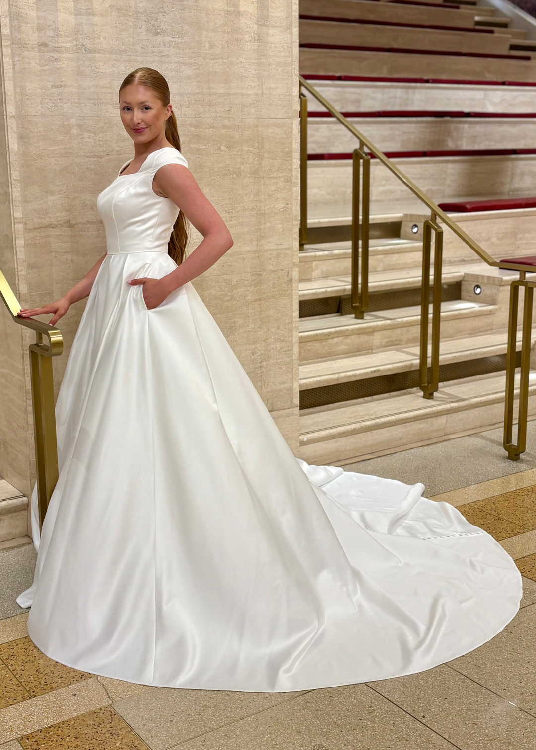Woman in a white modest wedding dress standing on a staircase in an elegant building.