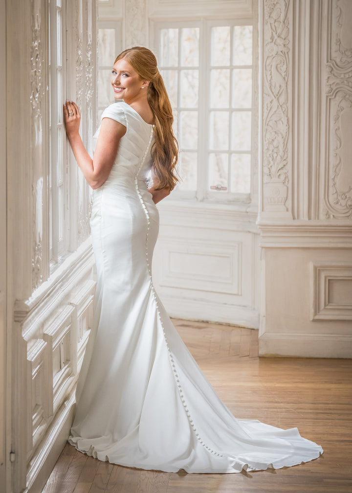 Woman in a white wedding dress standing in an elegant room with ornate walls.
