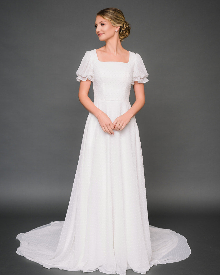 Woman wearing a modest
 wedding dress against a gray background