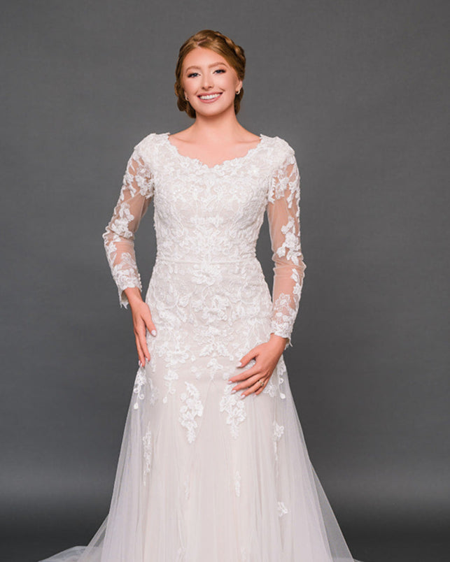 Woman wearing a modest ivory wedding dress with long sleeves against a dark background
