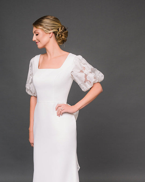 Woman wearing a modest wedding dress with floral sleeves against a dark background